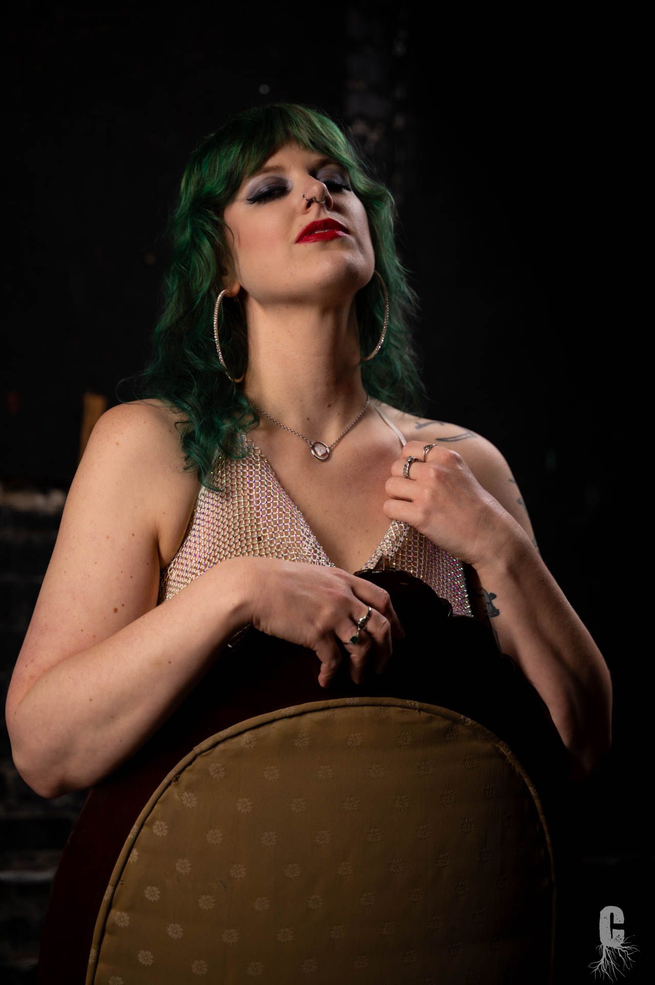 A glamor photo of a model looking down at the camera while straddling a chair