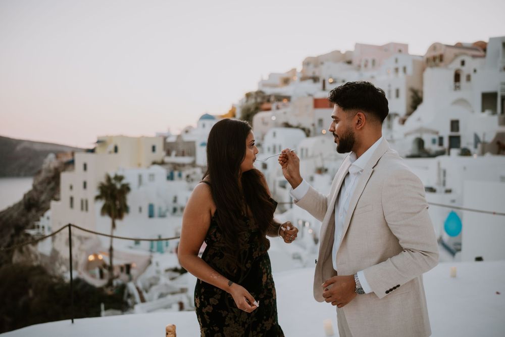 Romantic proposal moment on rooftop in Santorini with white buildings in background.