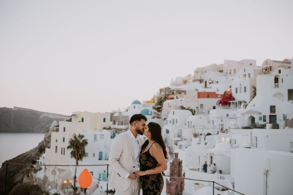 Romantic couple embracing on balcony with white Santorini architecture and sea view.