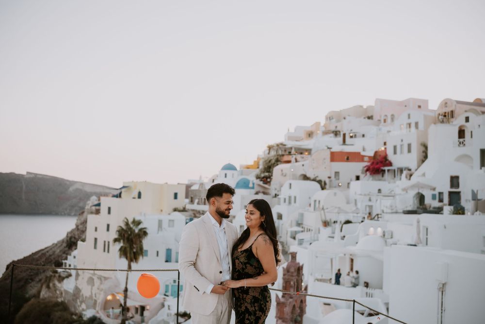 Intimate moment between couple against classic white buildings of Santorini at dusk.