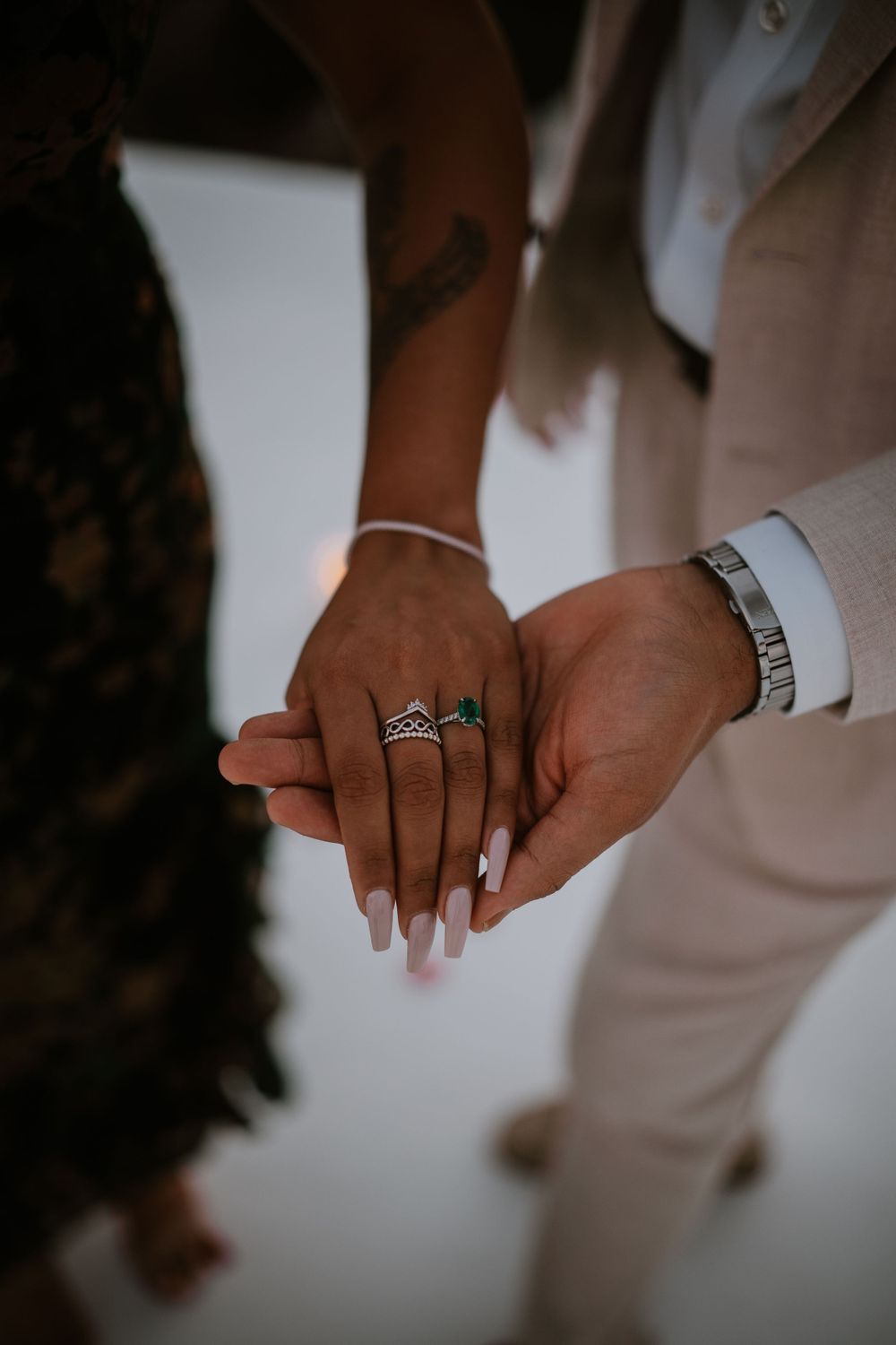 Close-up of hands showing engagement ring and wedding bands against white background.