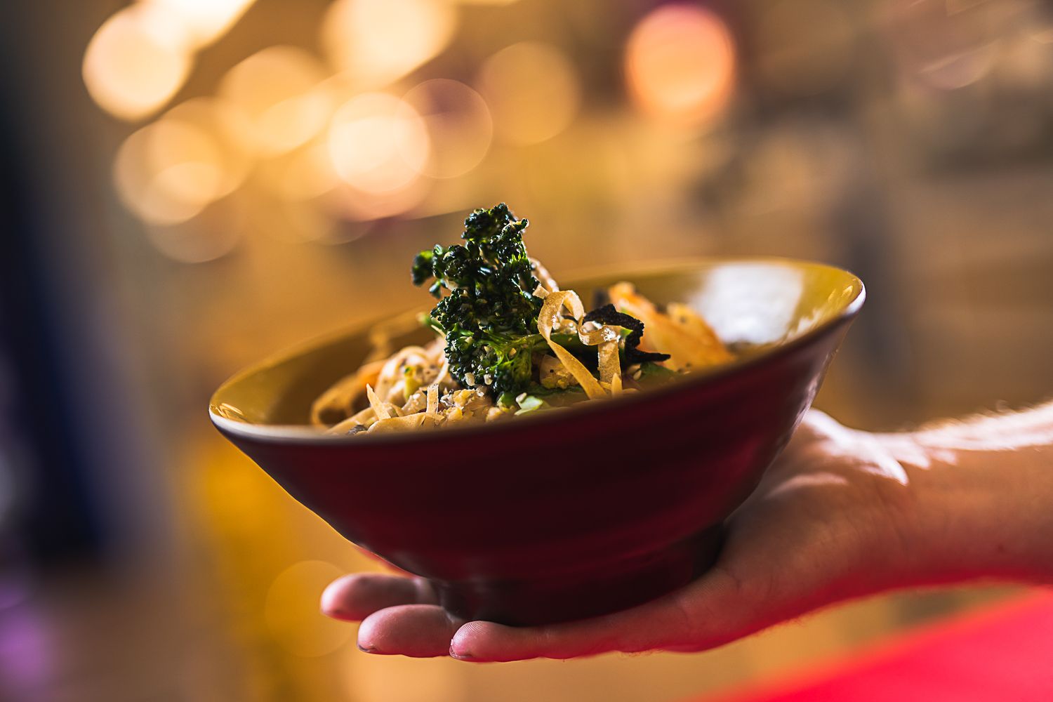 Restaurant chef plating an elegant Asian dish in a black bowl.