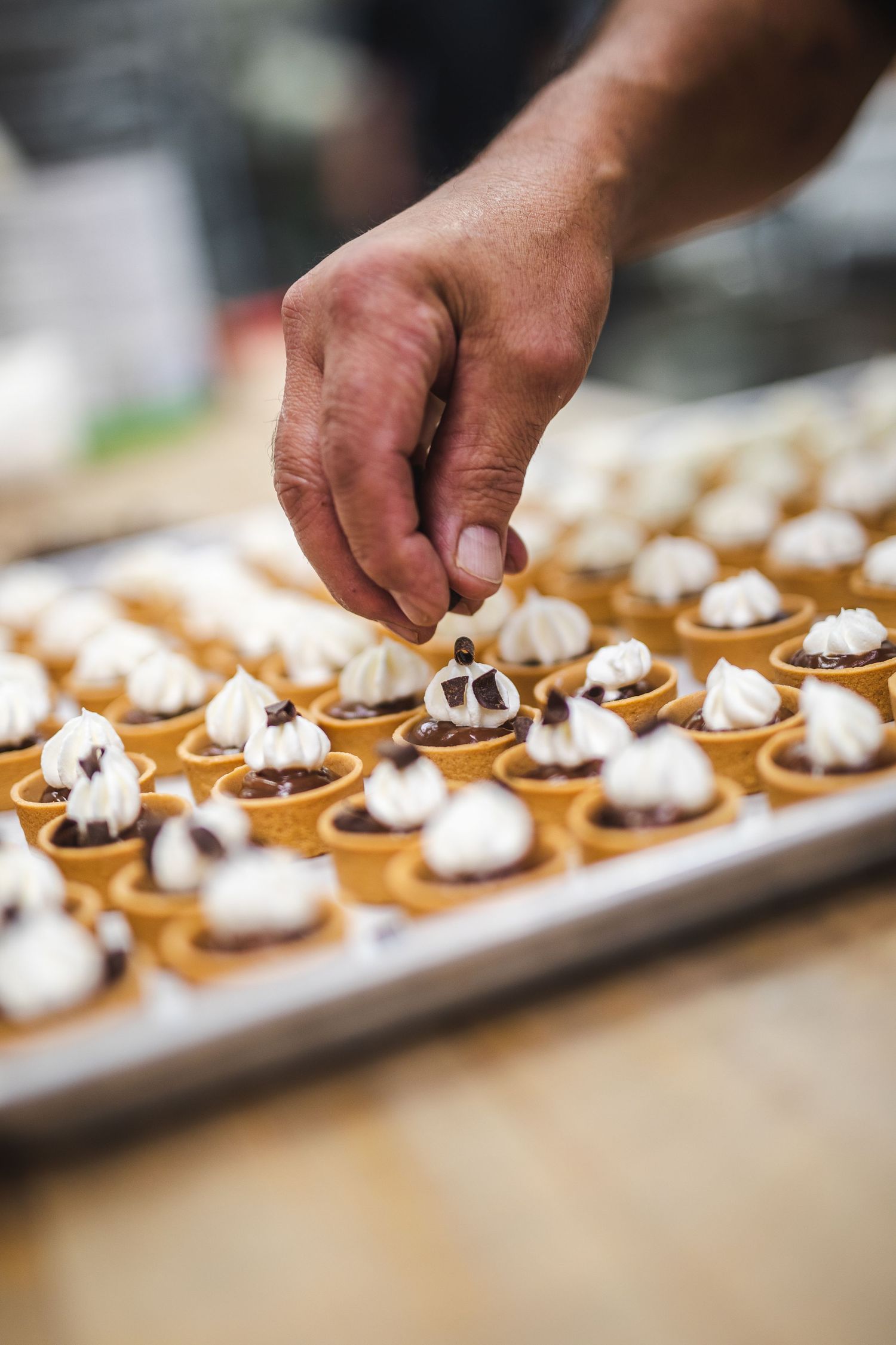 Hand placing decorative toppings on miniature dessert tarts filled with cream and chocolate.