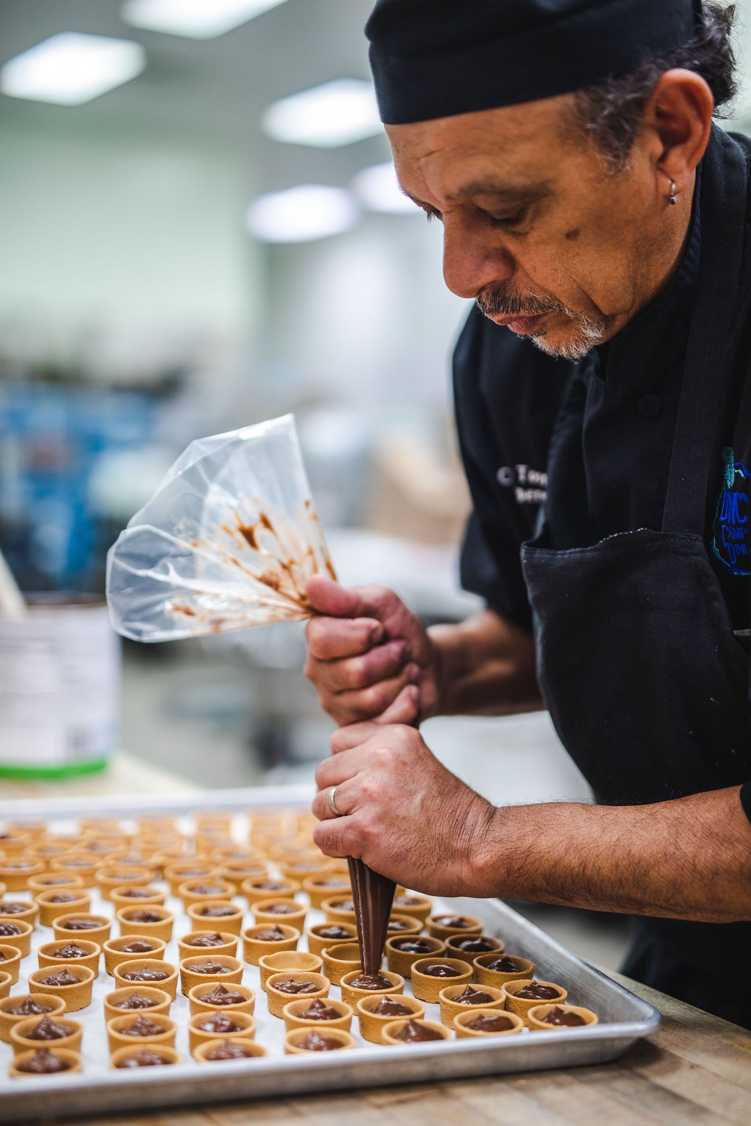 Pastry chef piping decorative toppings onto rows of desserts.