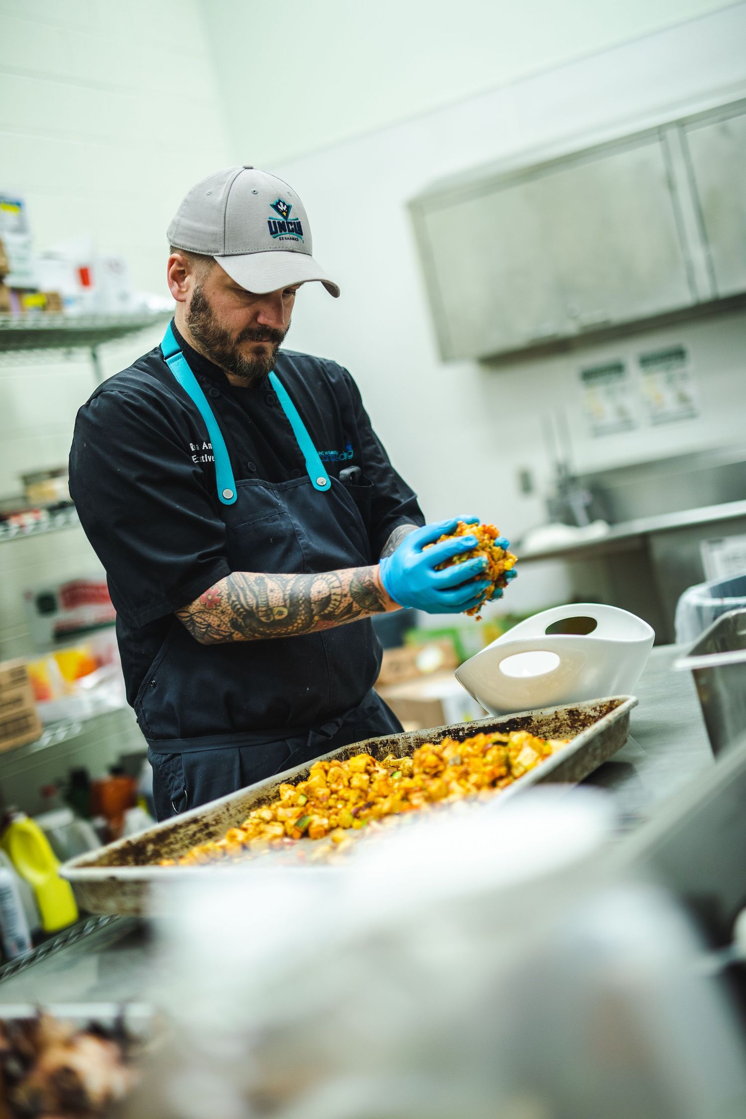 A kitchen worker in blue gloves preparing ingredients in a commercial kitchen setting.