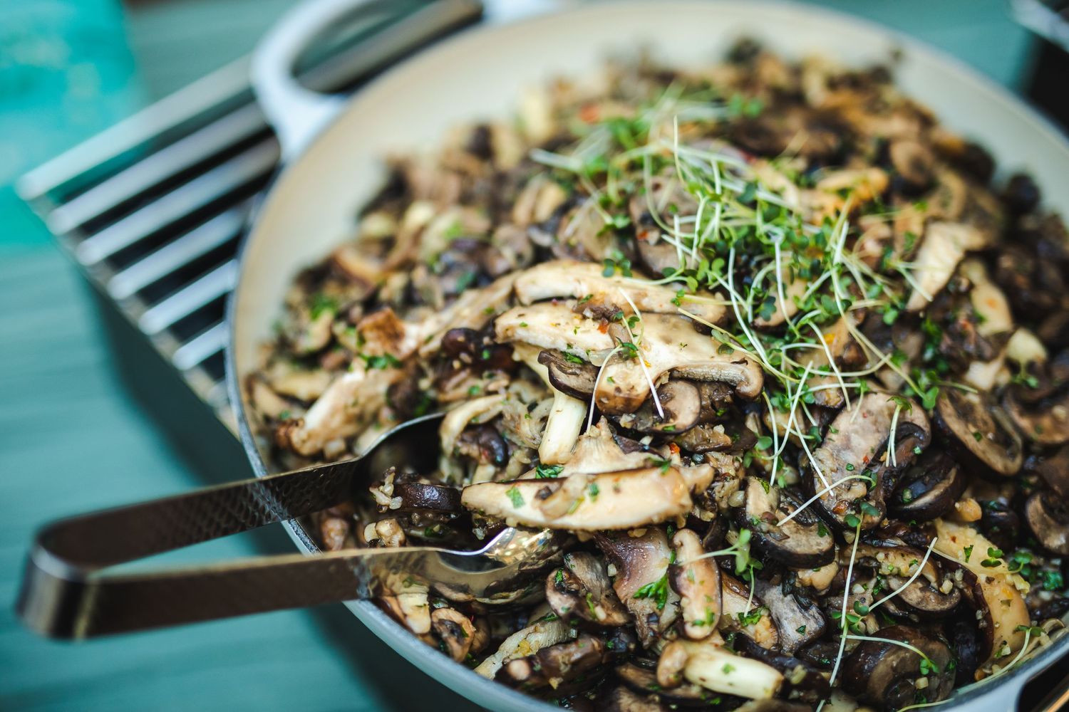 Sautéed mushroom and herb dish with fresh microgreen garnish in a large pan.