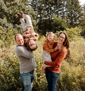 A playful family portrait with parents holding children outdoors in a sunny field.