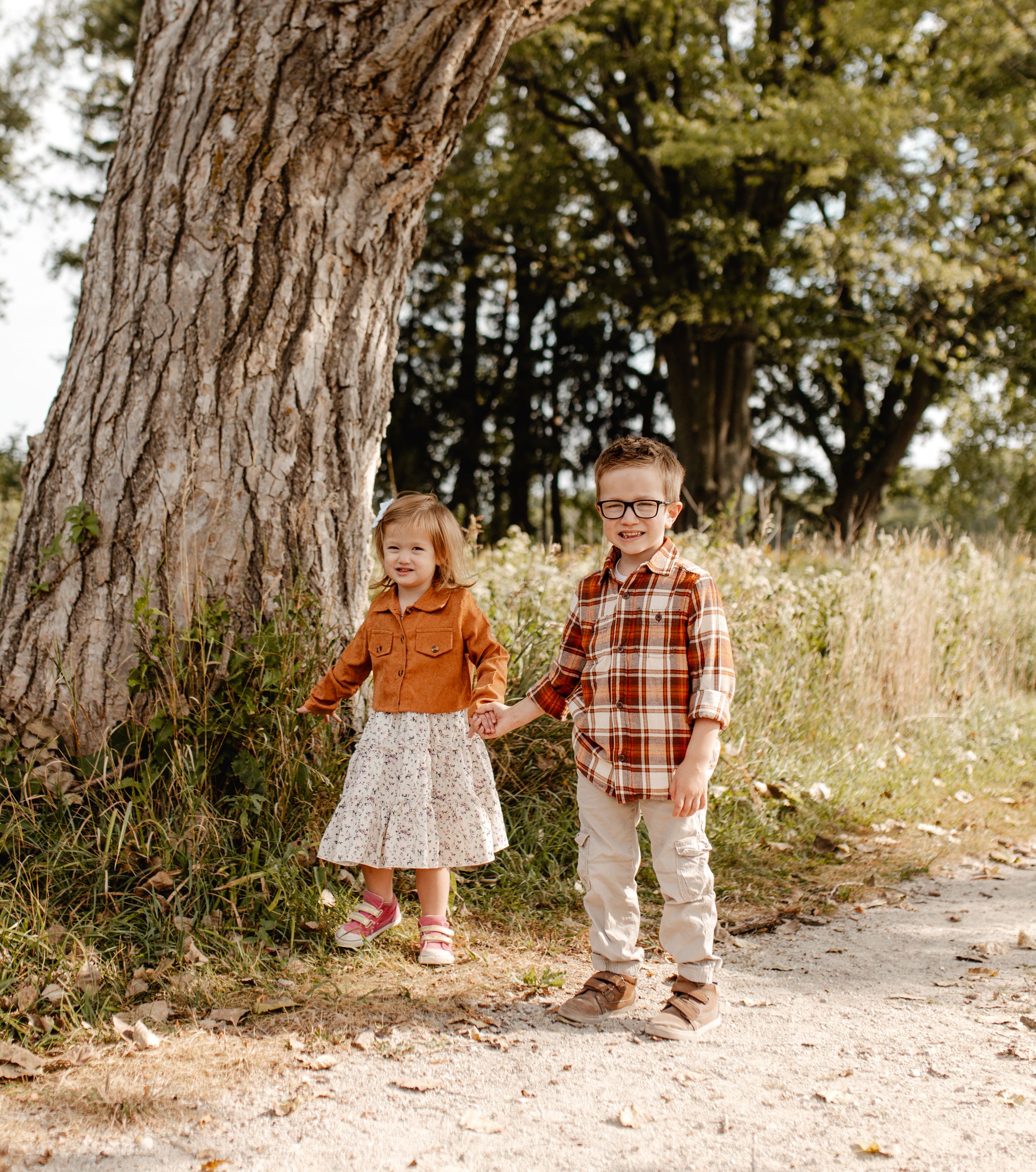 Two young children standing together under a large tree on a nature path.