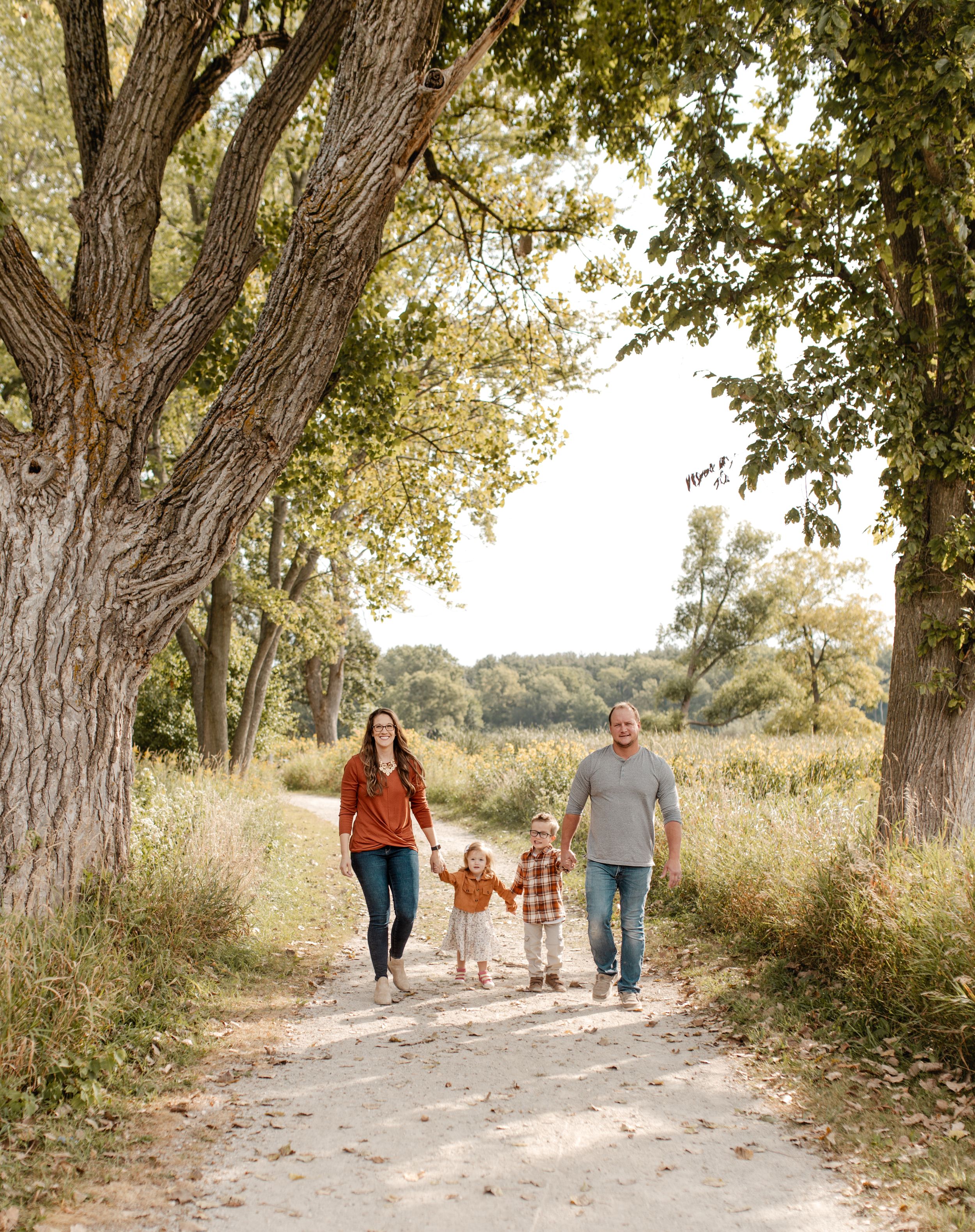 A family walking together on a tree-lined dirt path during autumn.