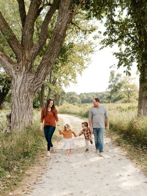 A joyful family swinging children while walking down a tree-lined path.