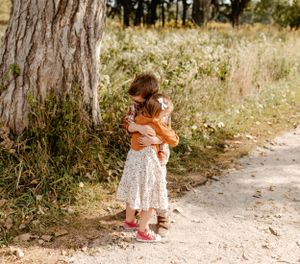 Two small children sharing a sweet hug beside a large tree trunk.