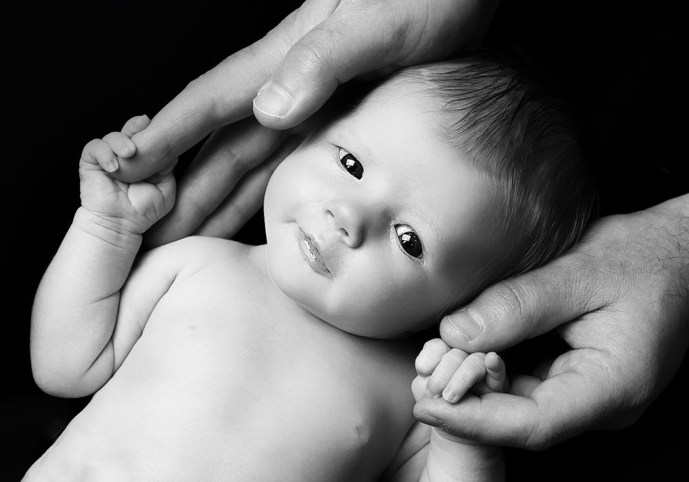 newborn baby held by dads hands in black and white