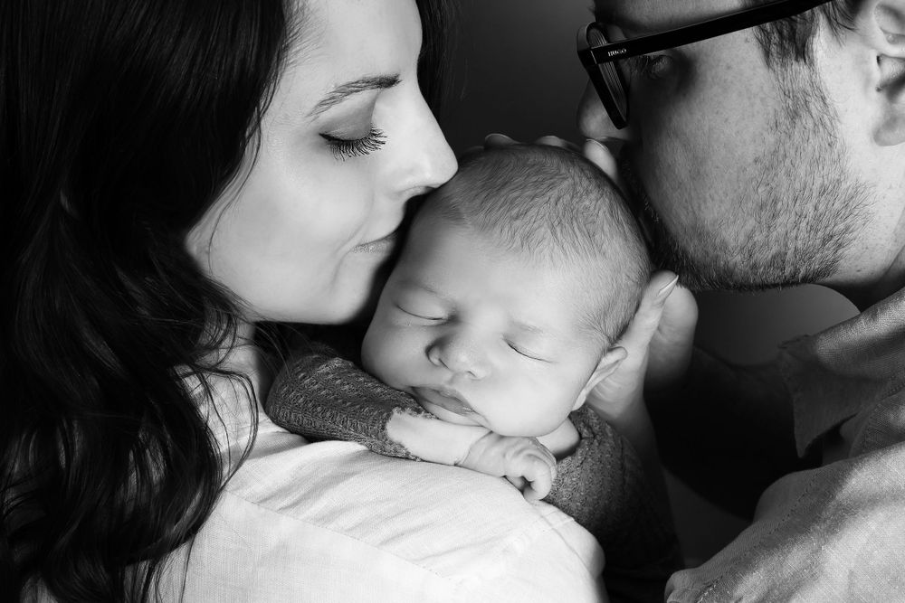 newborn baby on mums shoulder with mum and dad kissing baby