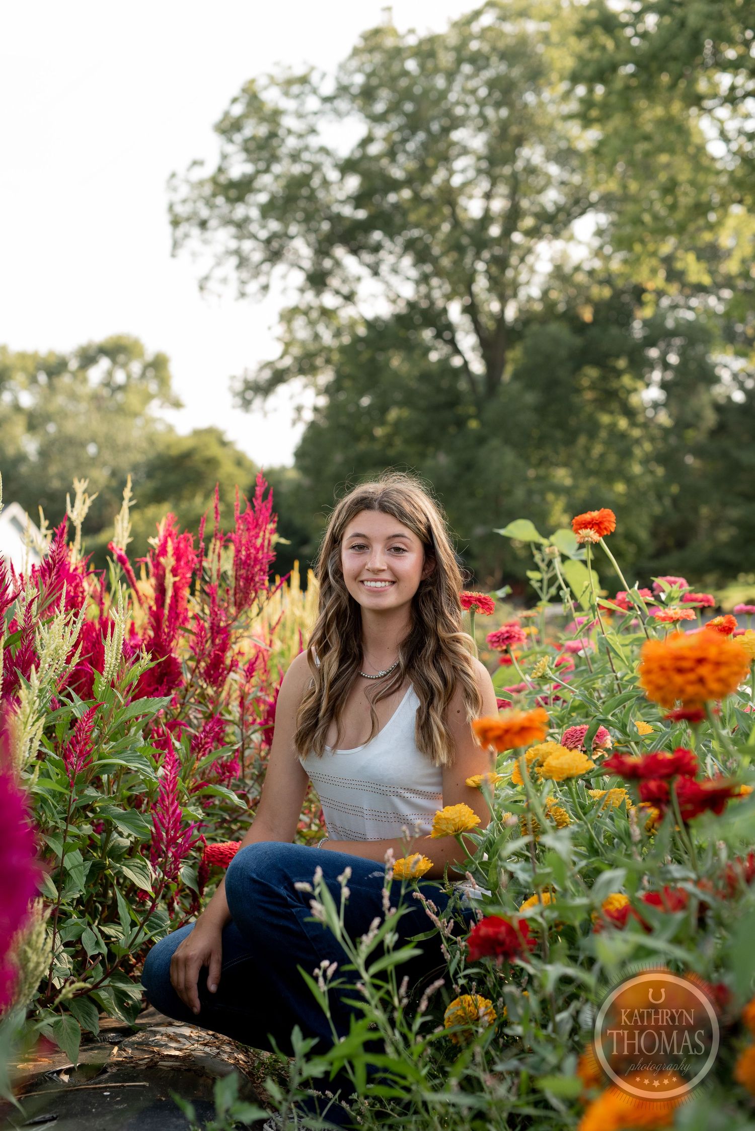 A person kneels among bright orange and red flowers in a lush summer garden.