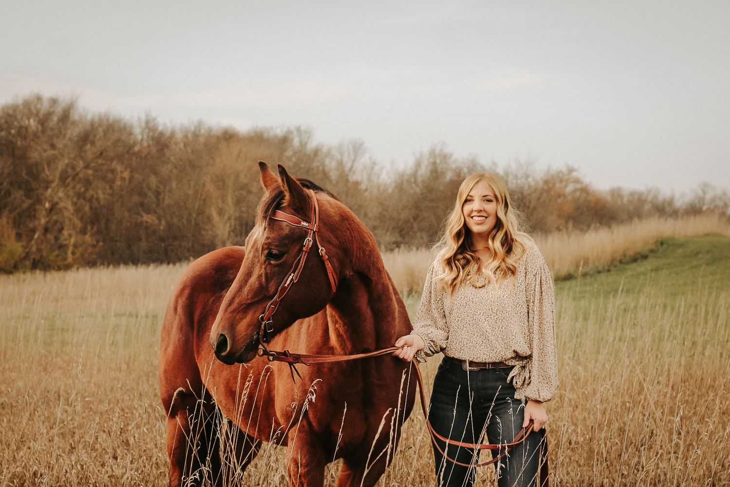 A chestnut horse stands in a grassy field during golden hour with its handler.