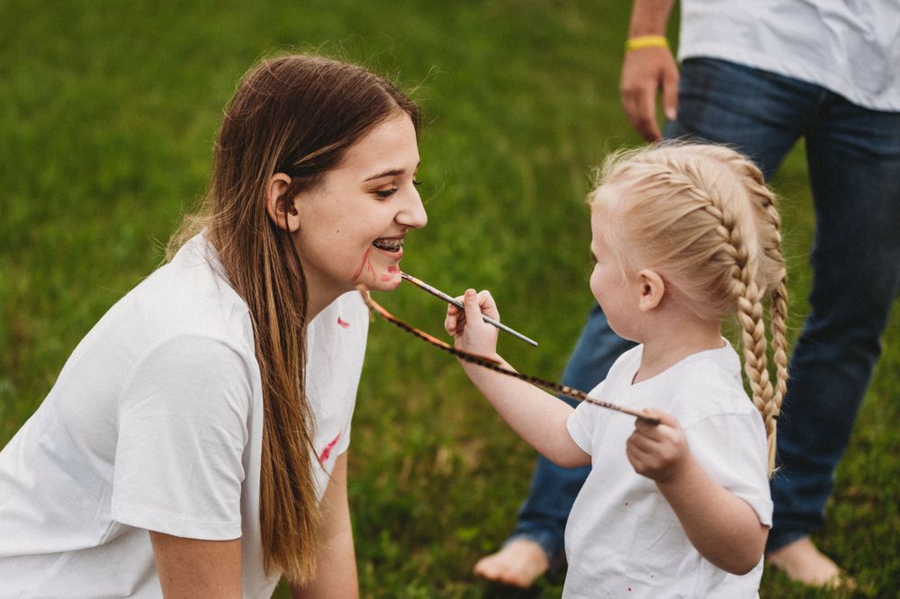 Playful face painting moment outdoors on a sunny day.