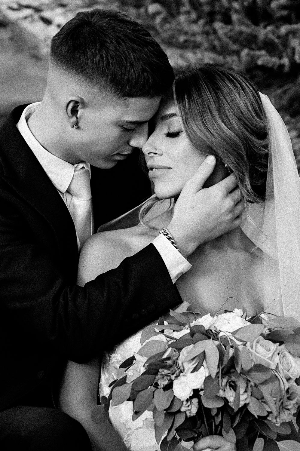 An intimate black and white portrait of a couple sharing a tender moment with a bridal bouquet.