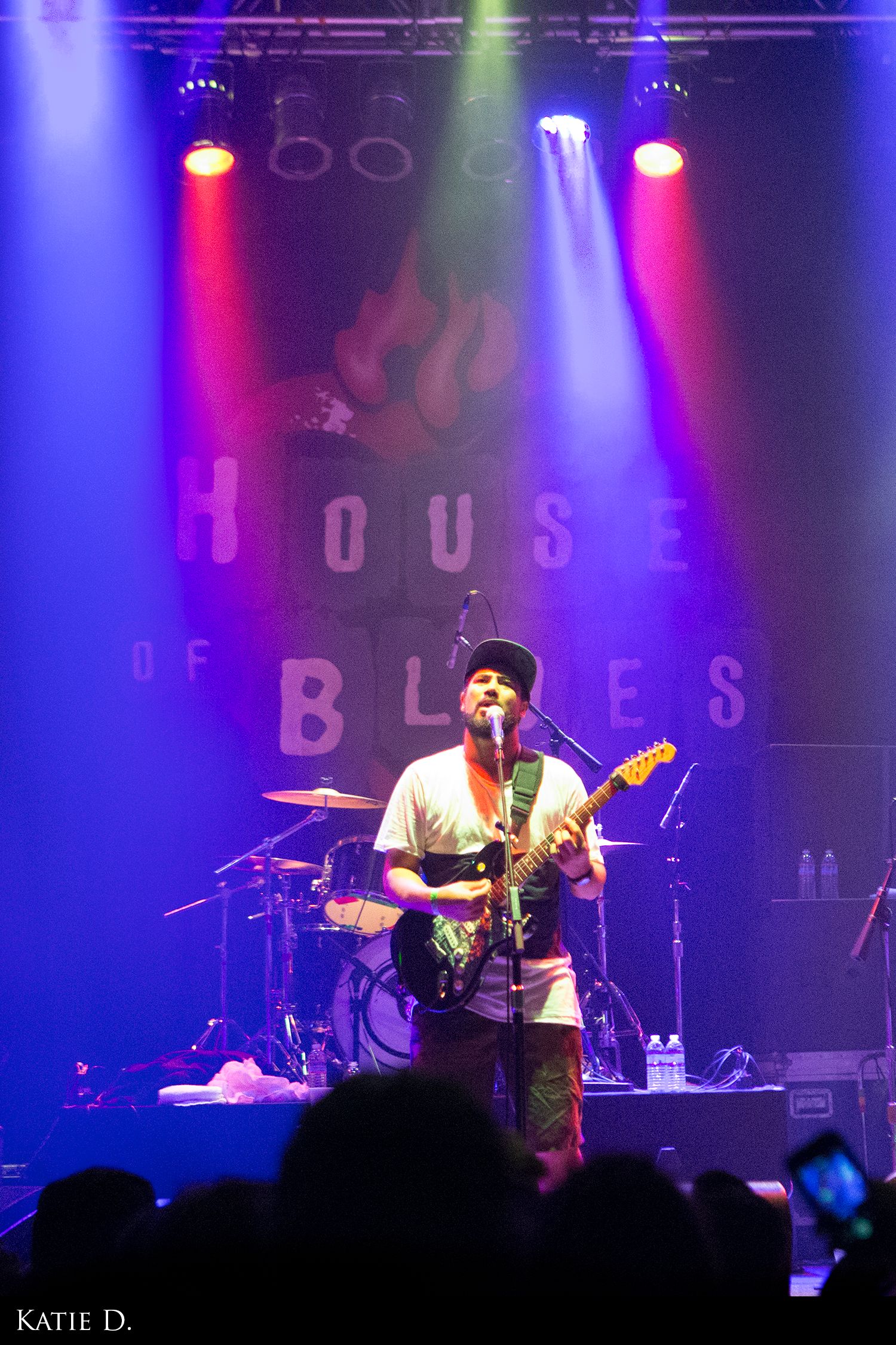 Guitarist performing on stage at House of Blues under colorful concert lighting.