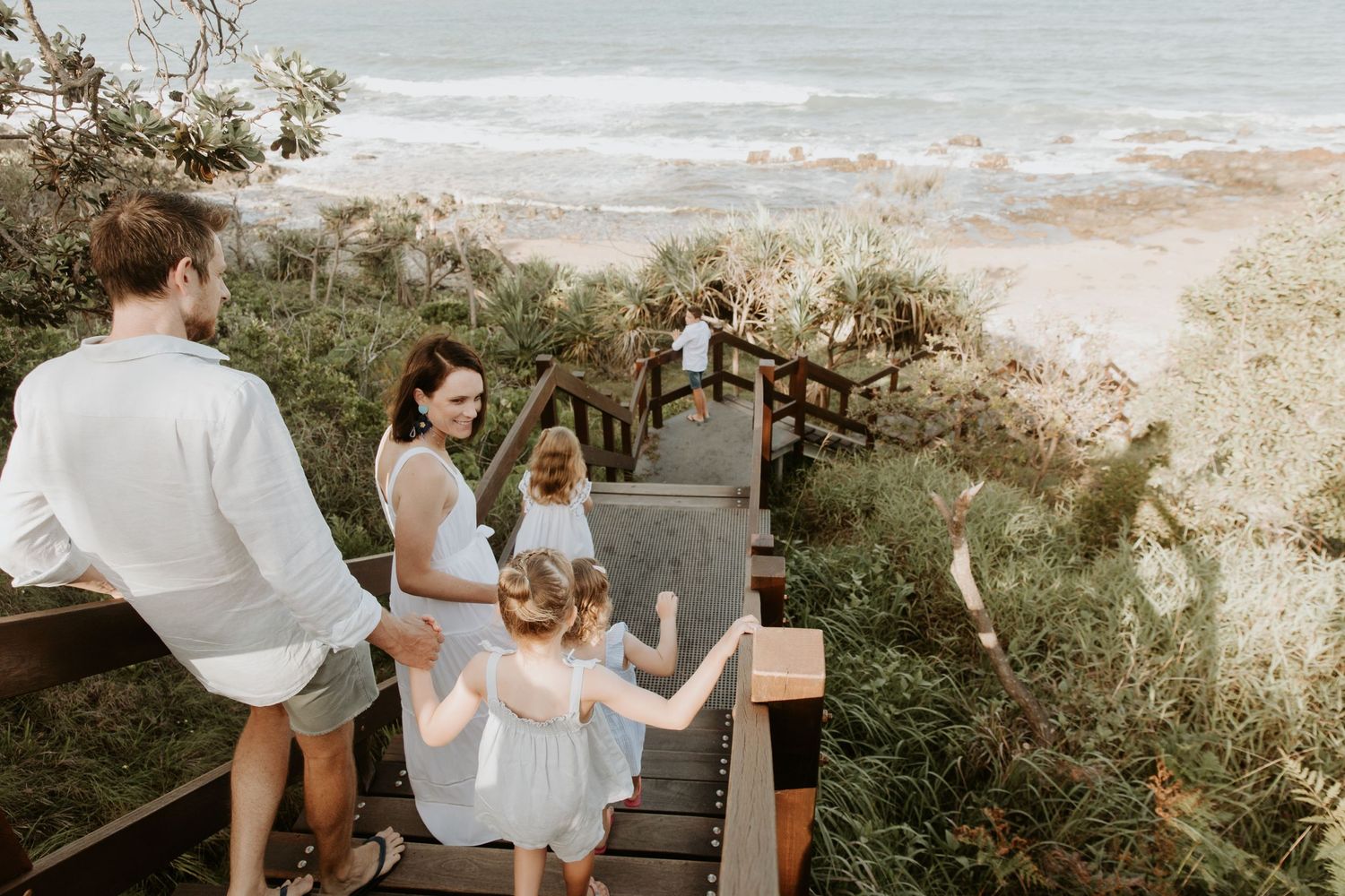 beautifully dressed family of six with four young children walking down timber stairs to the beach