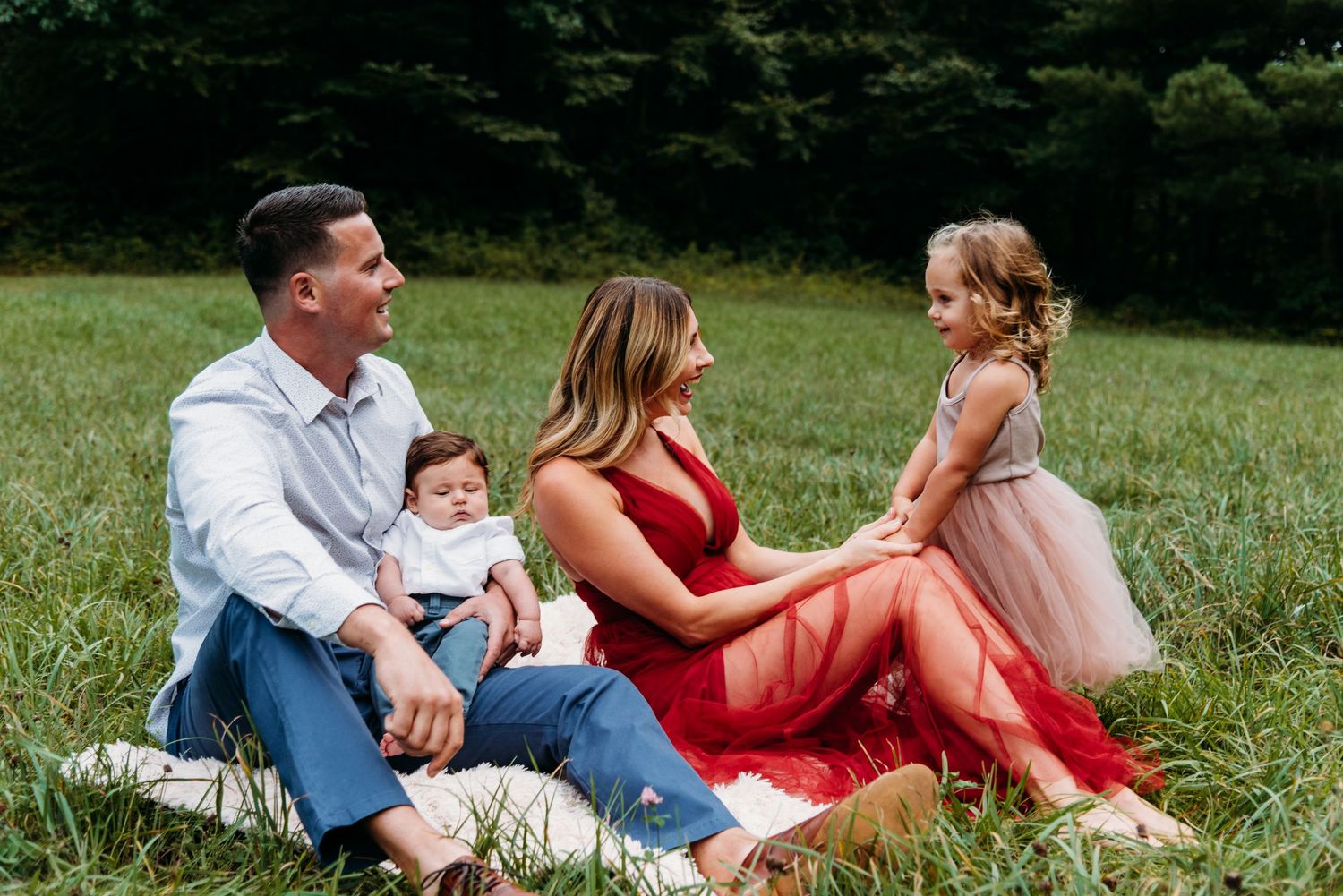 Family sitting together on blanket in grassy field wearing formal attire.
