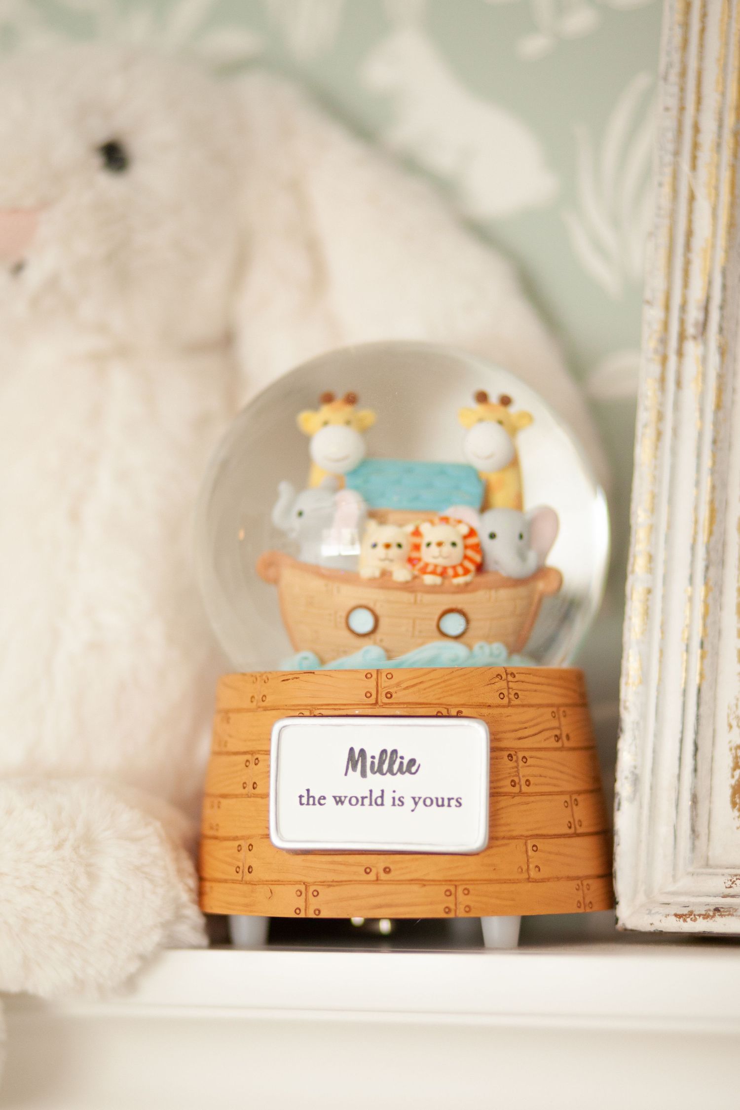 A Noah's Ark themed musical snow globe with cute animals sitting on a wooden base labeled 'Hello' on a white shelf.