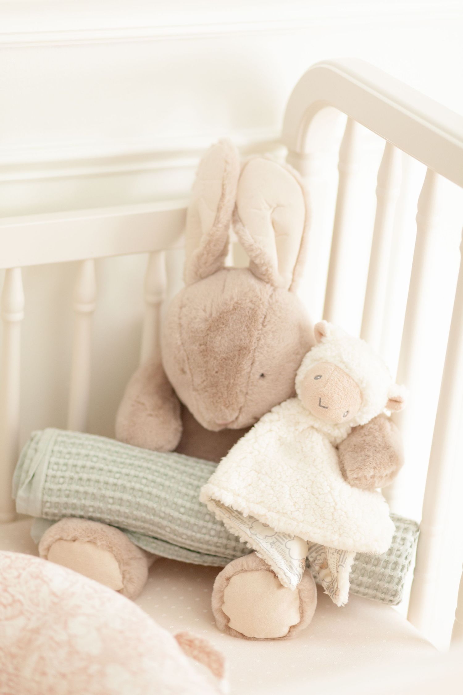 Soft plush toys and knitted items rest on a white rocking chair, creating a cozy nursery corner in muted pastel tones.