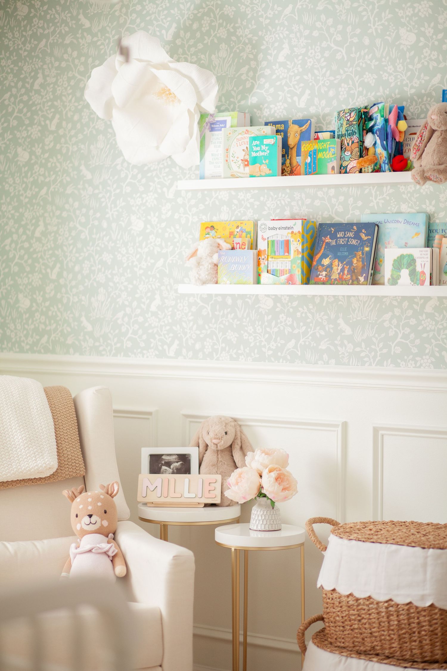 Cozy nursery corner with floating bookshelves, plush toys, and woven basket storage against soft wallpapered walls.