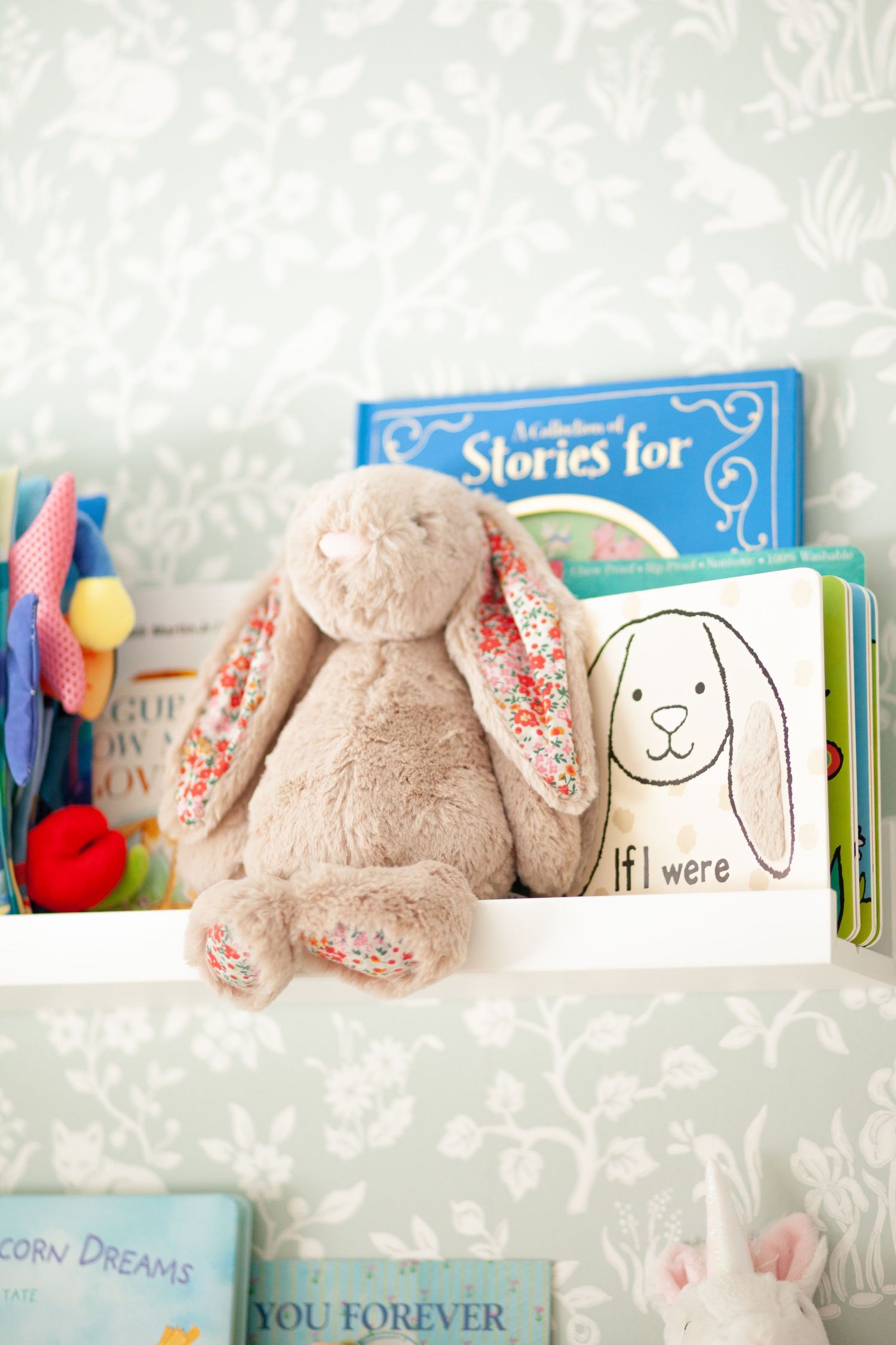 A soft plush bunny with floral patterned ears sits on a shelf next to children's storybooks and colorful toys.