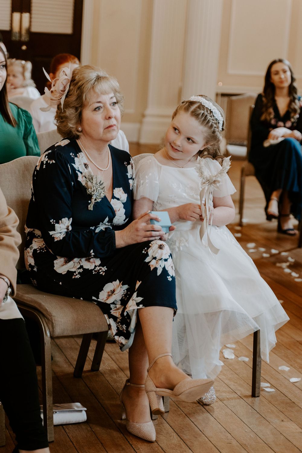 a flower sitting with her nan at a wedding. she is looking at her nan and smiling.
