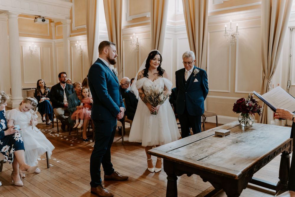 a bride and groom standing at the aisle. The brides dad is smiling