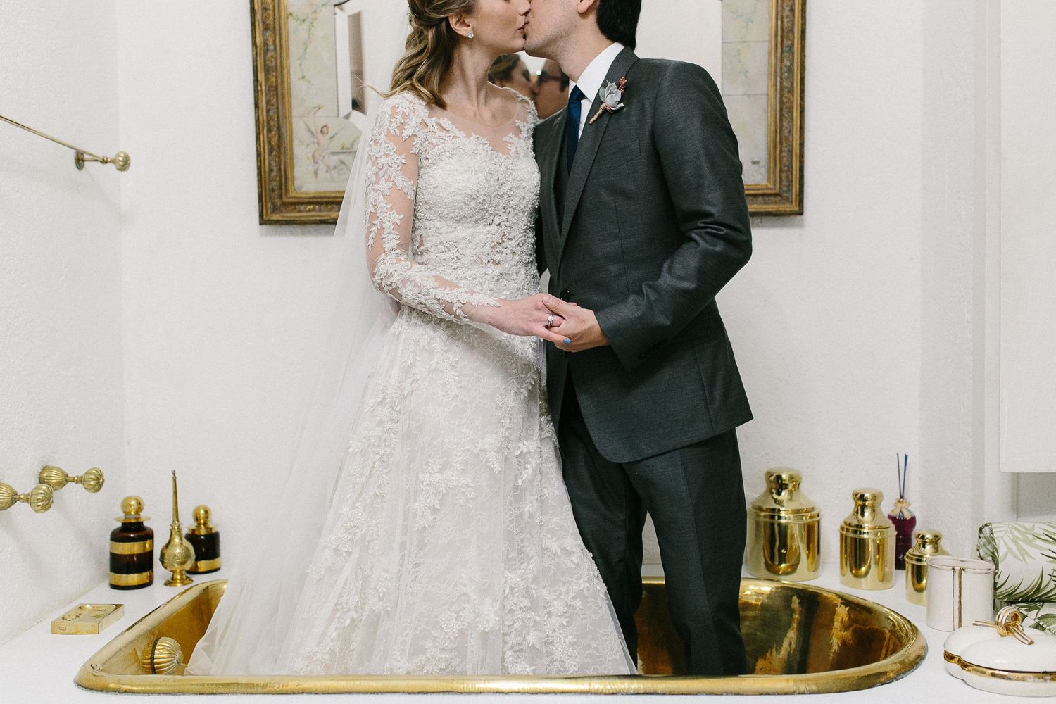 Elegant couple embracing in formal attire by ornate gold mirror.
