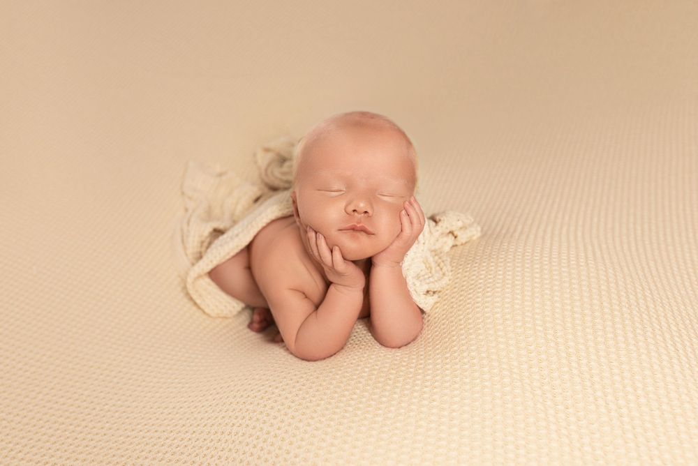 Peaceful sleeping newborn in cream wrap posed with hands under chin.