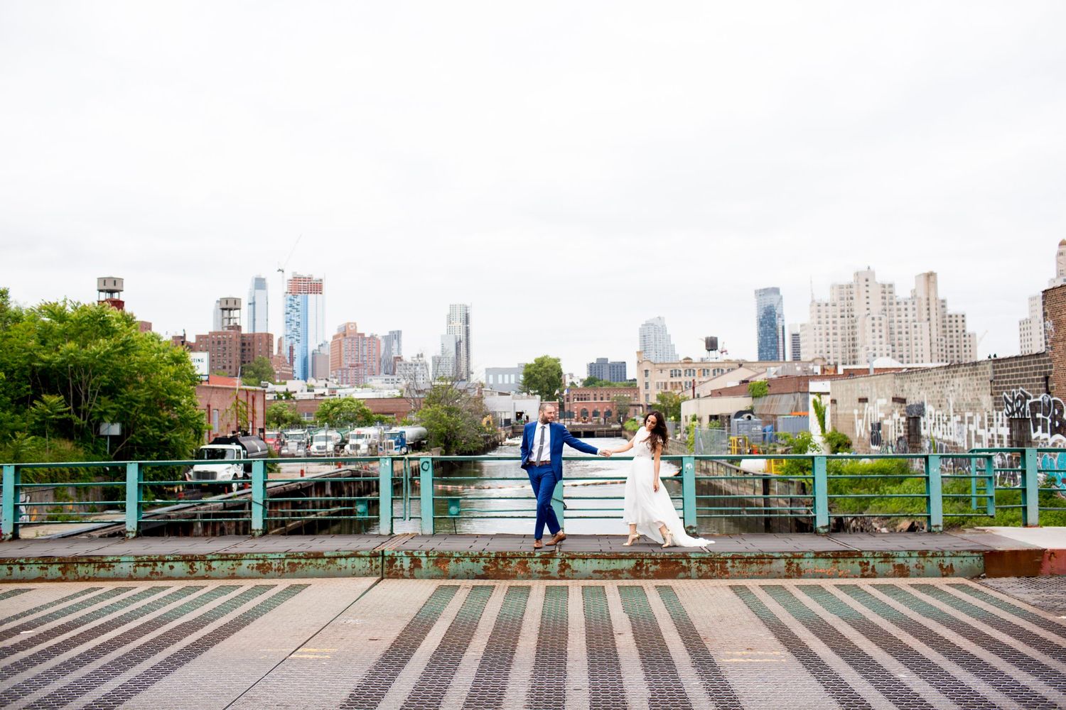 Wedding couple poses on urban boardwalk with city skyline backdrop.