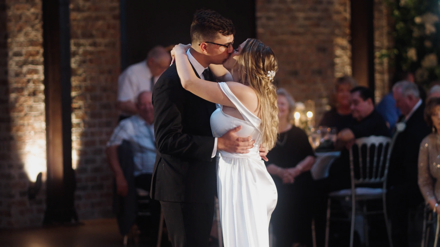 A couple shares their first dance in a dimly lit brick venue.