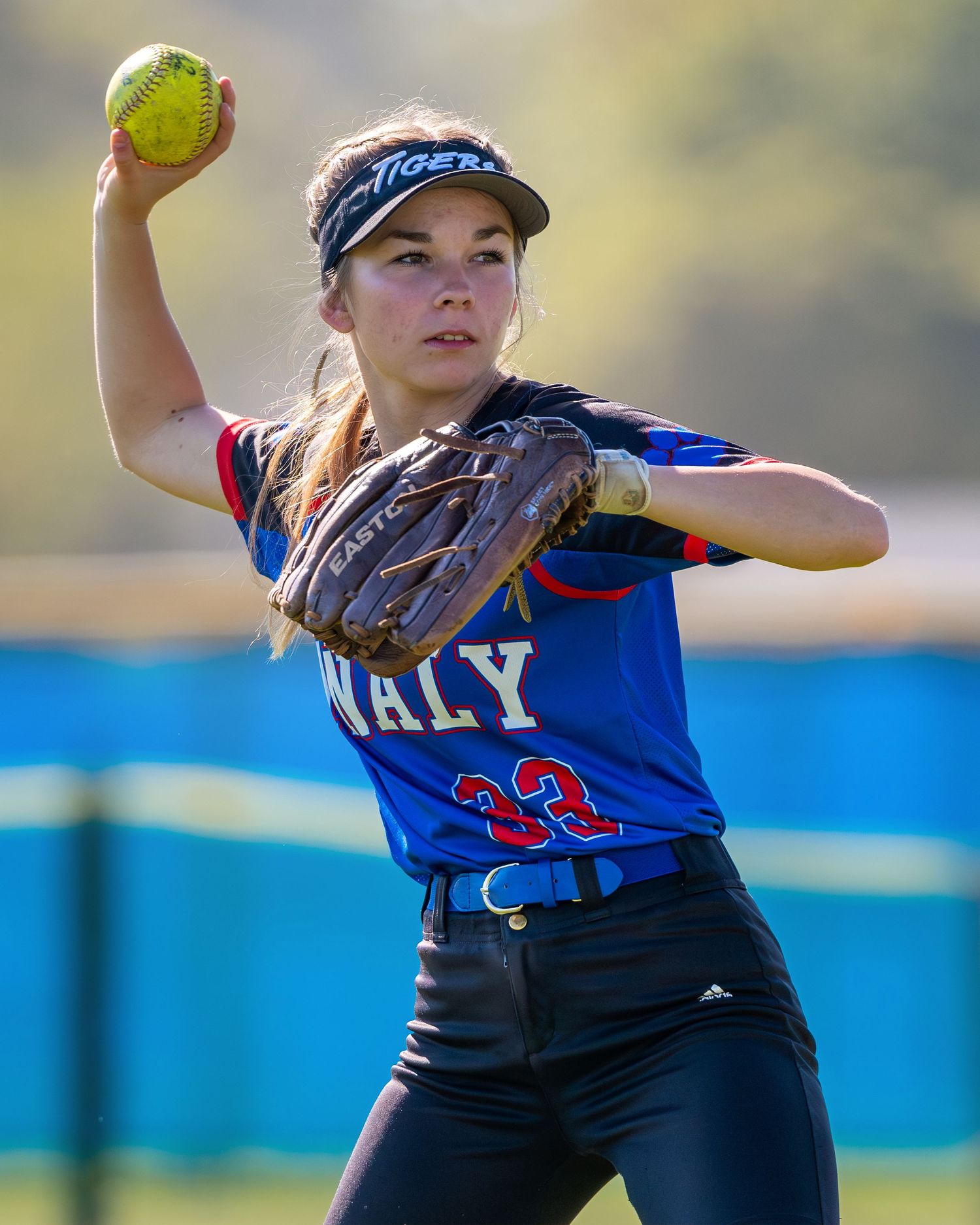 Softball pitcher in blue uniform mid-throw with yellow ball during game.