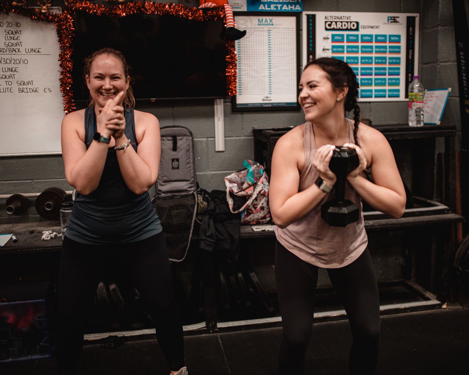 Two people laughing together while sitting on gym equipment during a workout session.