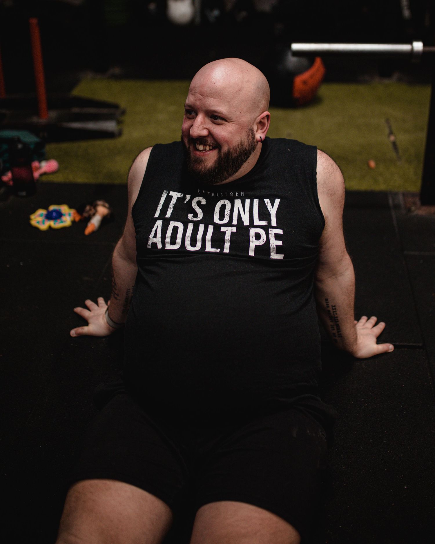 Person lifting a barbell overhead while wearing pink shorts and a gray tank top in a home gym.