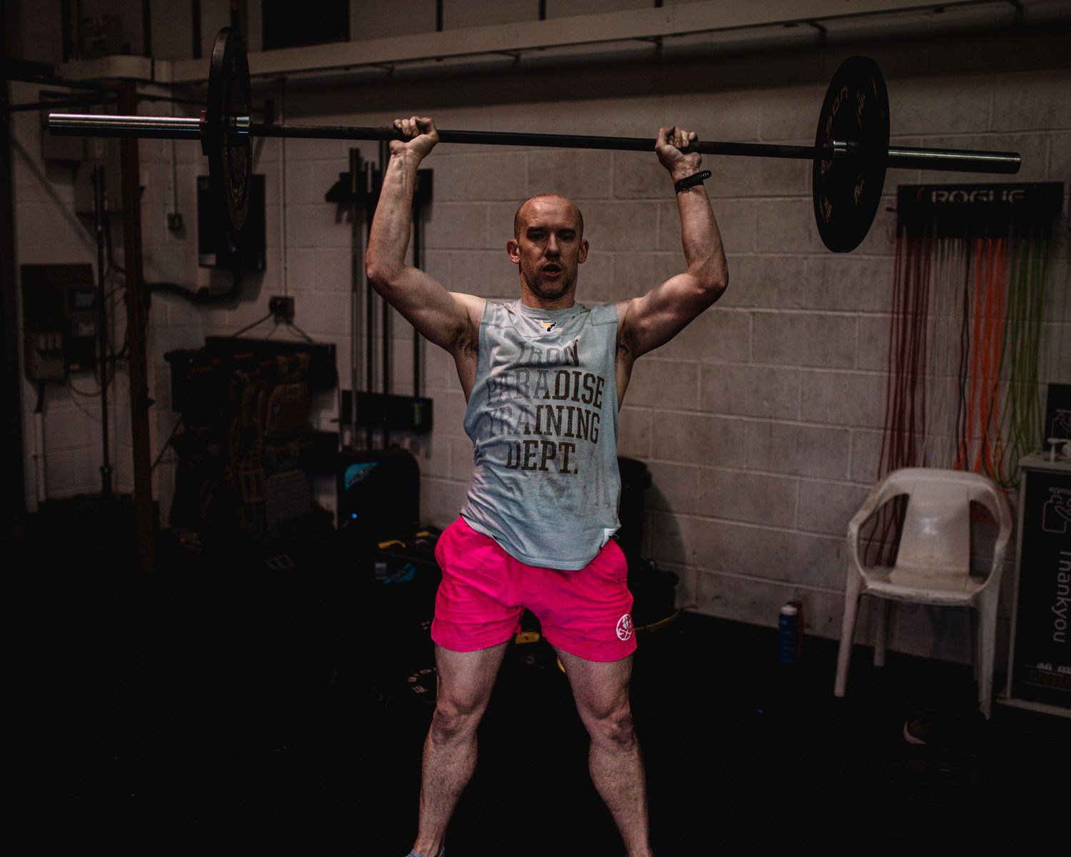 Athlete in black workout gear performing a stretching exercise in a dark gym setting.
