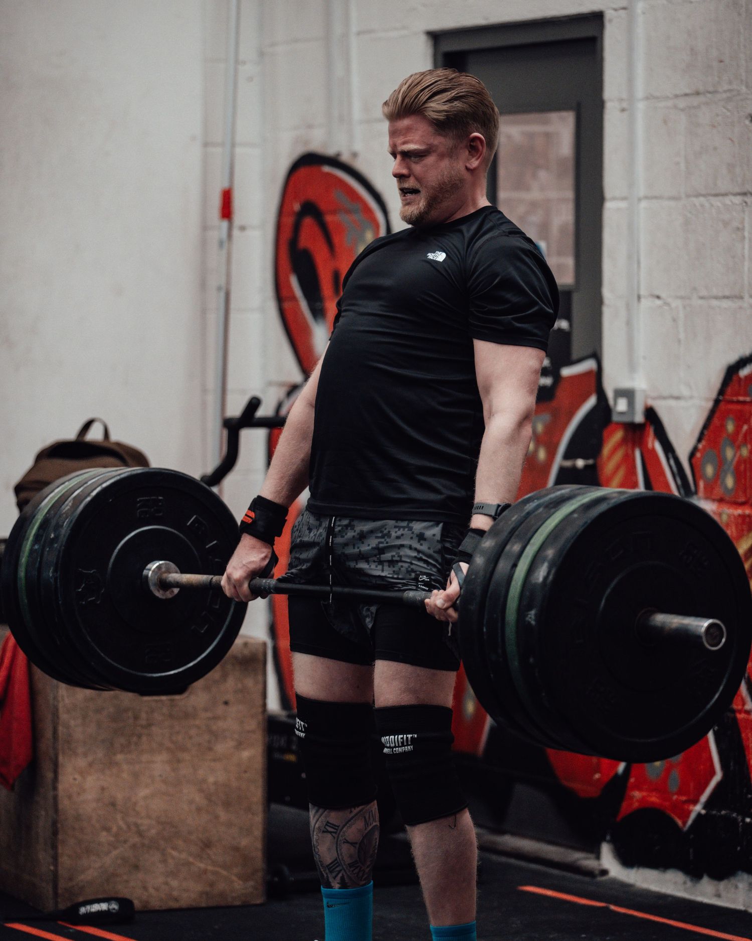 Person in black attire performing barbell deadlift with multiple weight plates in gym setting.