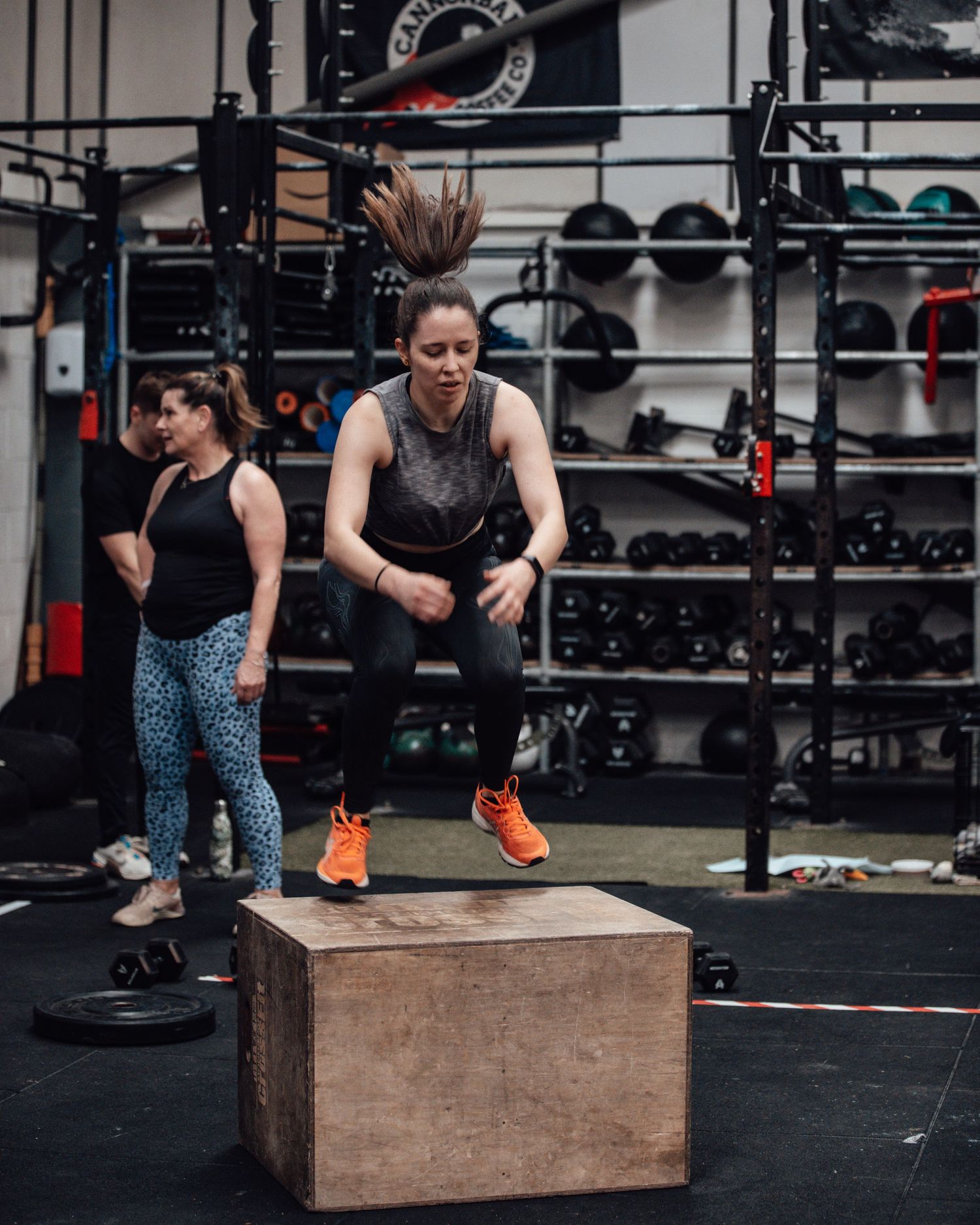Athletes training in a CrossFit gym with box jumps and equipment racks in the background.