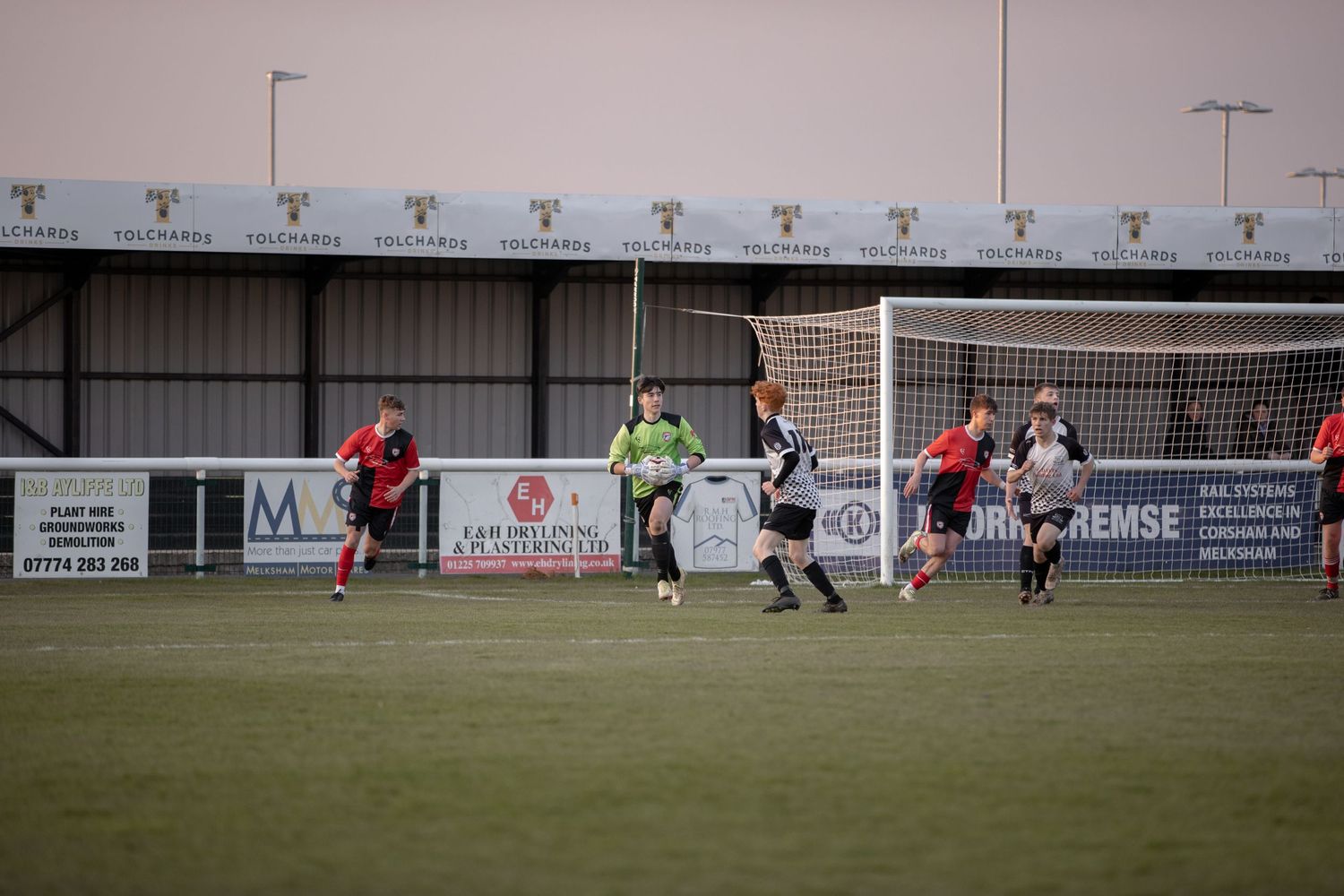 Soccer match action near goal with players from opposing teams competing for the ball.