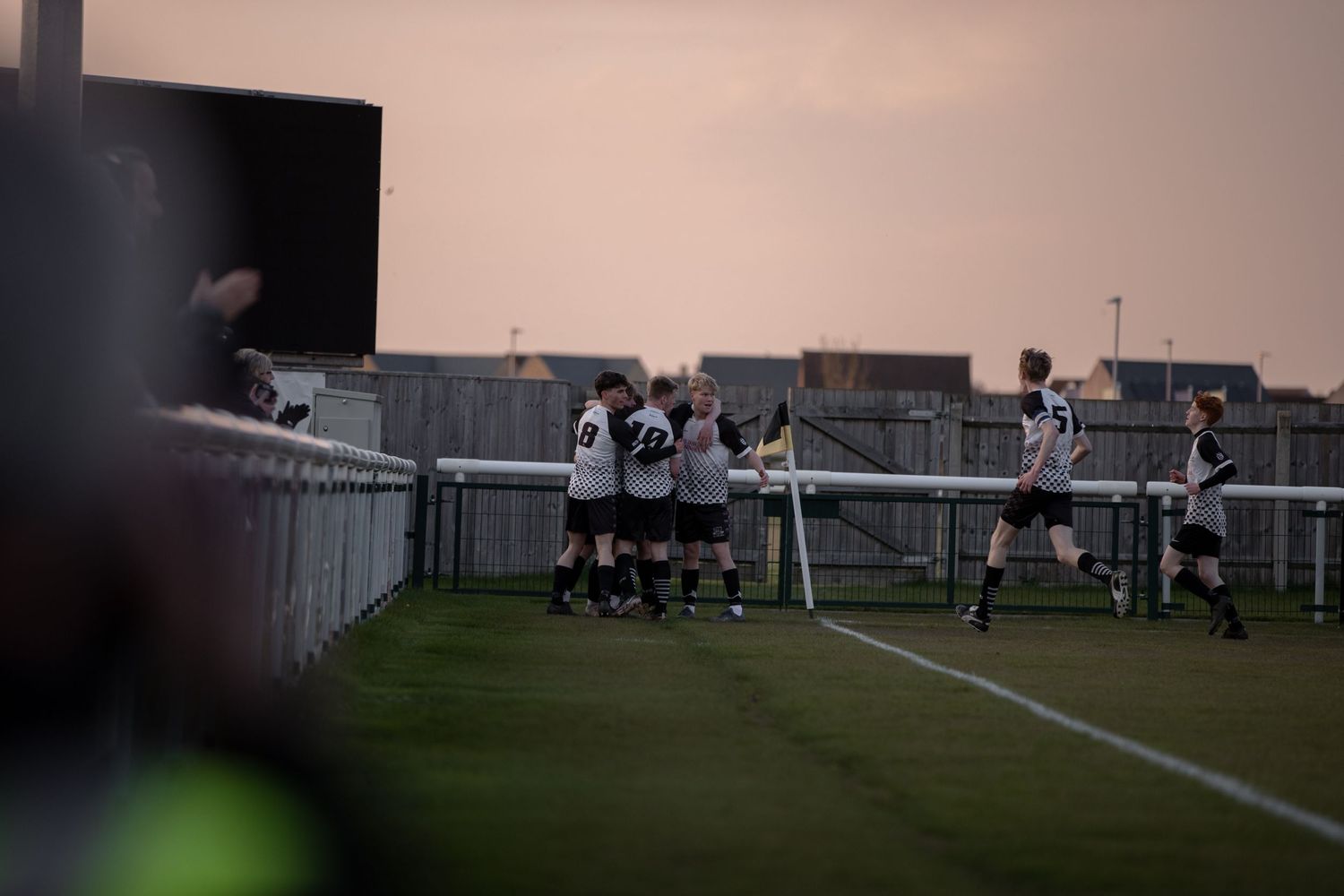 Players lined up defensively at the edge of a soccer field during dusk.