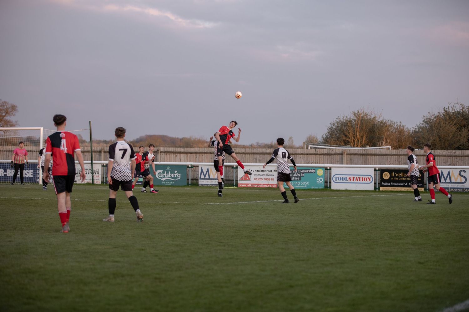 Soccer players jumping for header during competitive match on grass field.