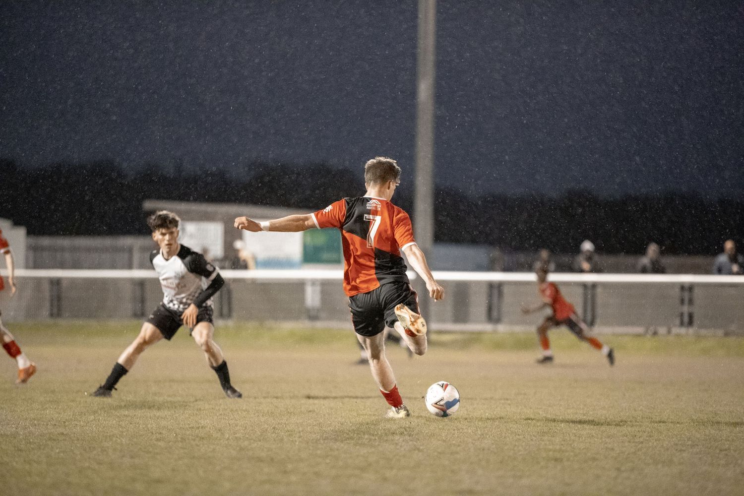 Soccer player in orange jersey dribbling ball during nighttime match.