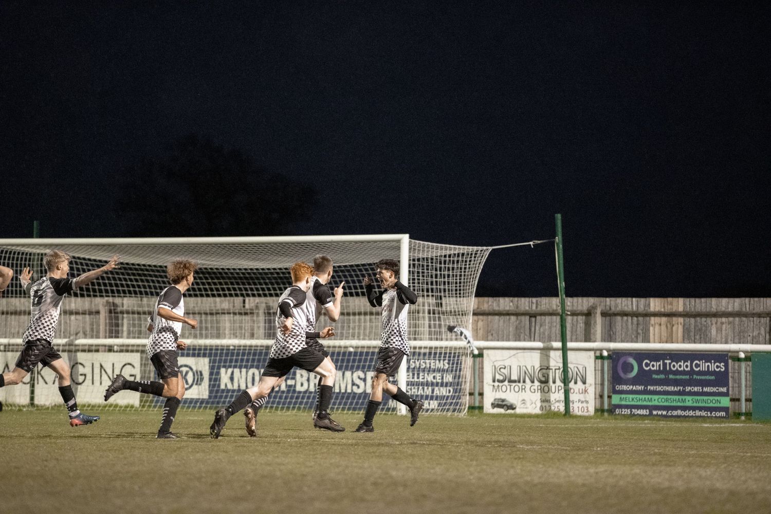 Soccer players jumping in unison to defend against a corner kick during a nighttime match.