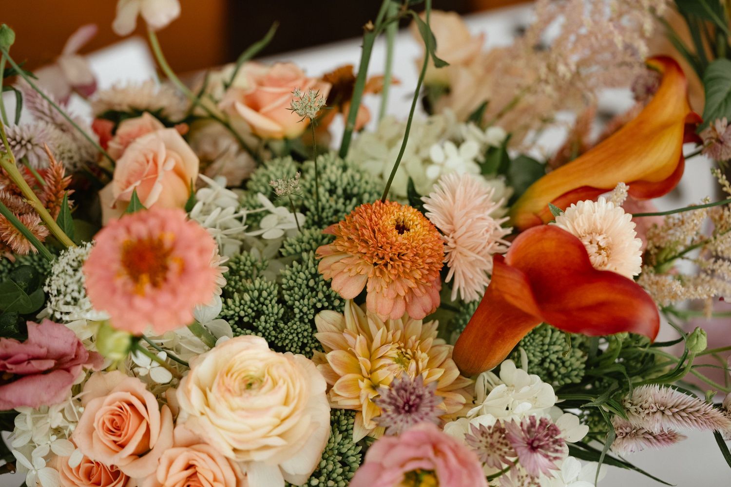 Romantic peach and coral flower arrangements with roses and dahlias on a table setting.