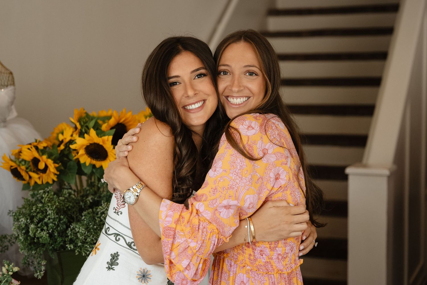 Two friends share a joyful embrace at a wedding celebration with sunflowers in the background.