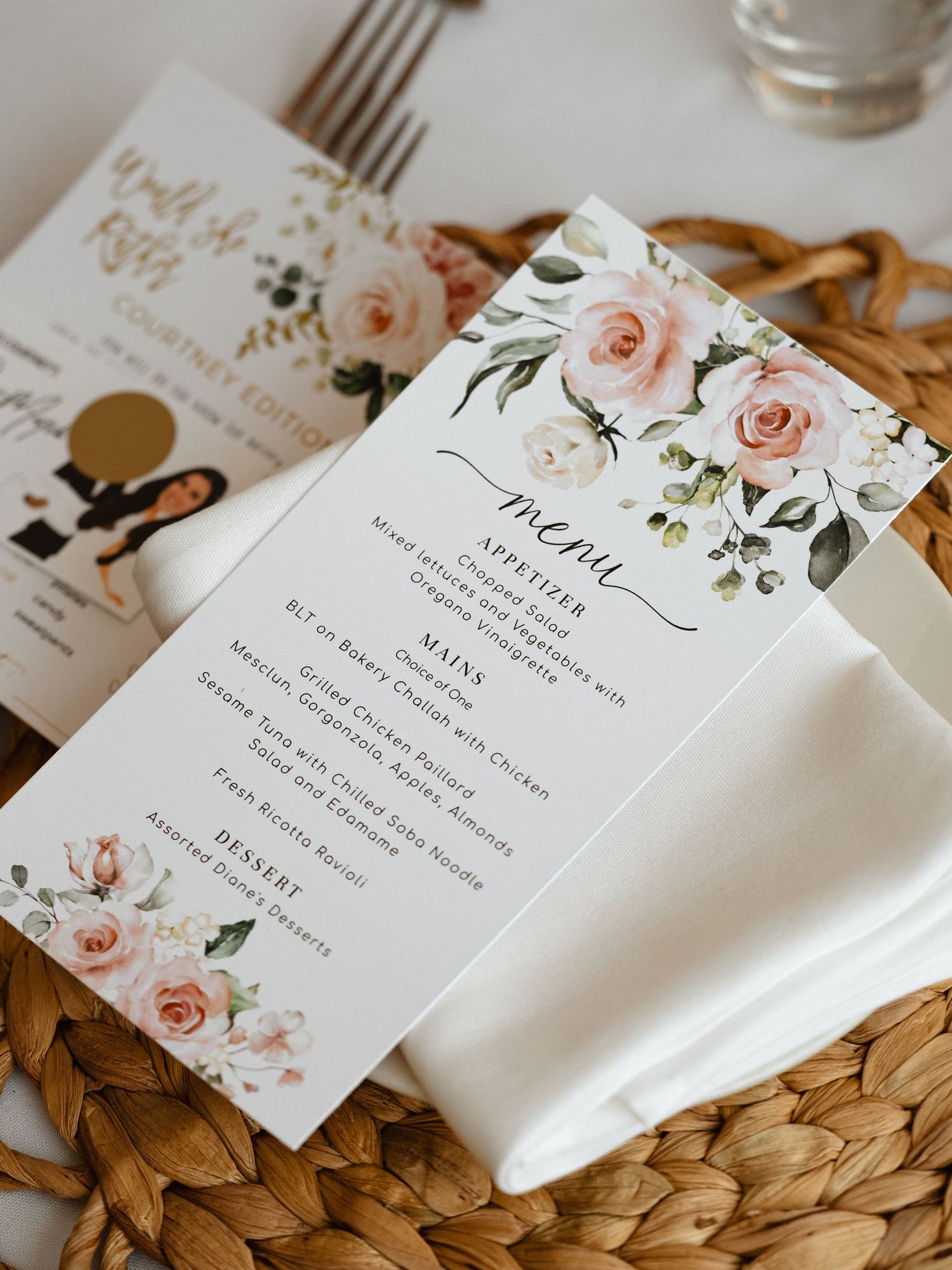 Wedding menu cards decorated with pink roses and greenery on woven placemats.