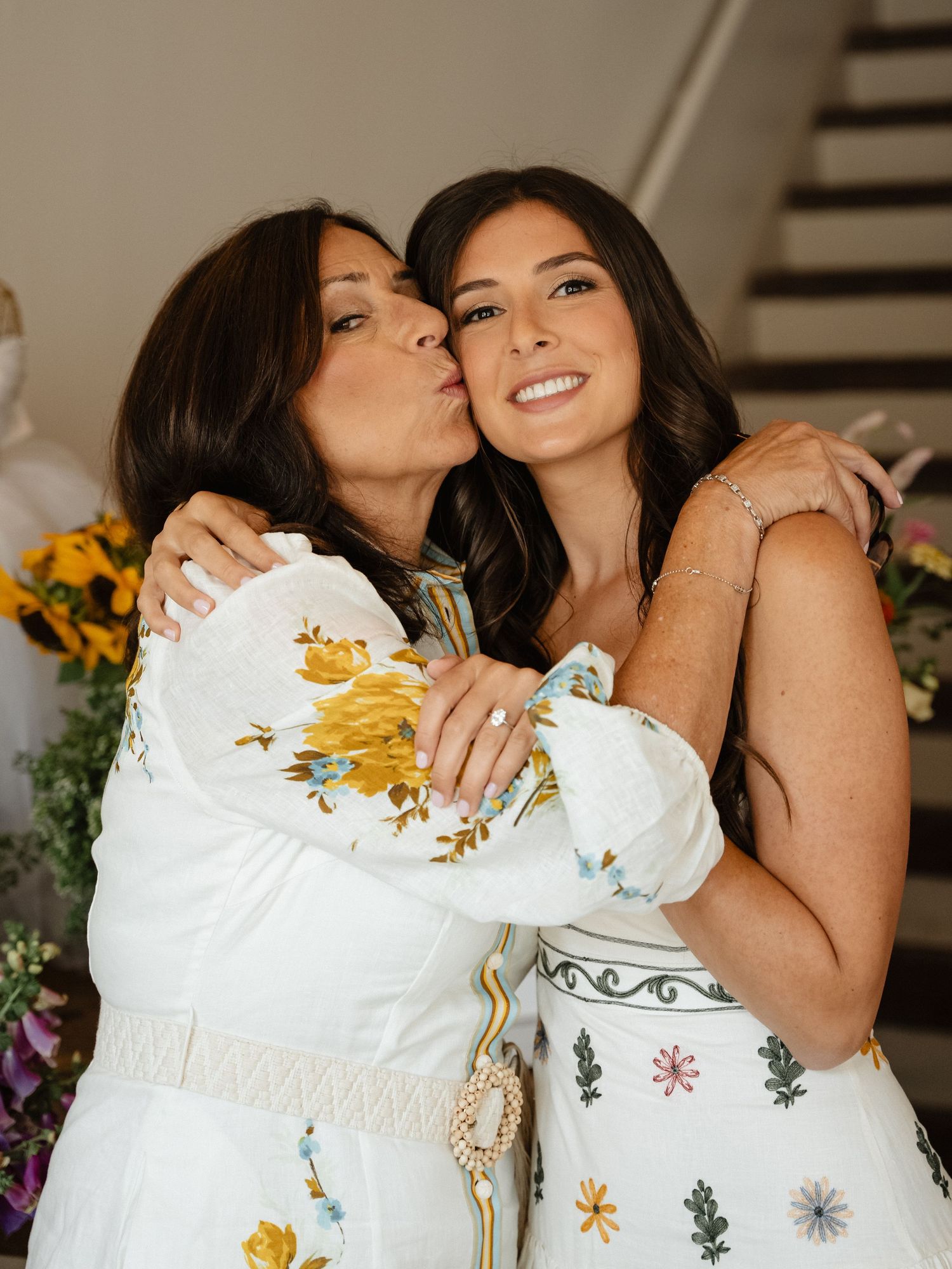 Women in white floral dresses sharing joyful moments at a celebration.