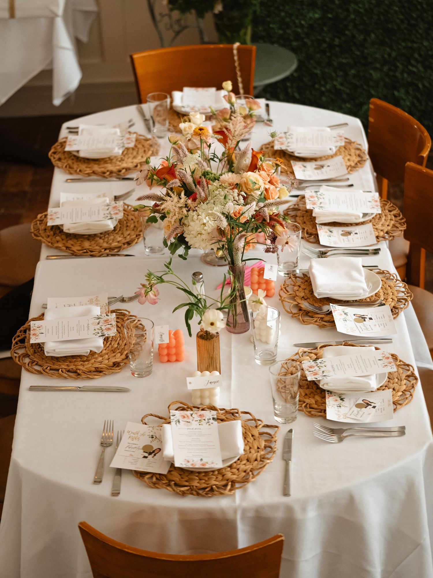 Long dining table set with woven chargers and elegant place settings for a celebration.